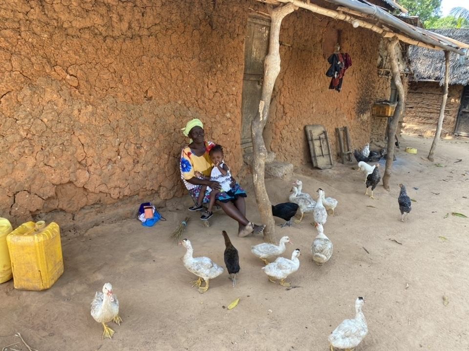 Mother with Daughter on lap with a couple of chickens running around